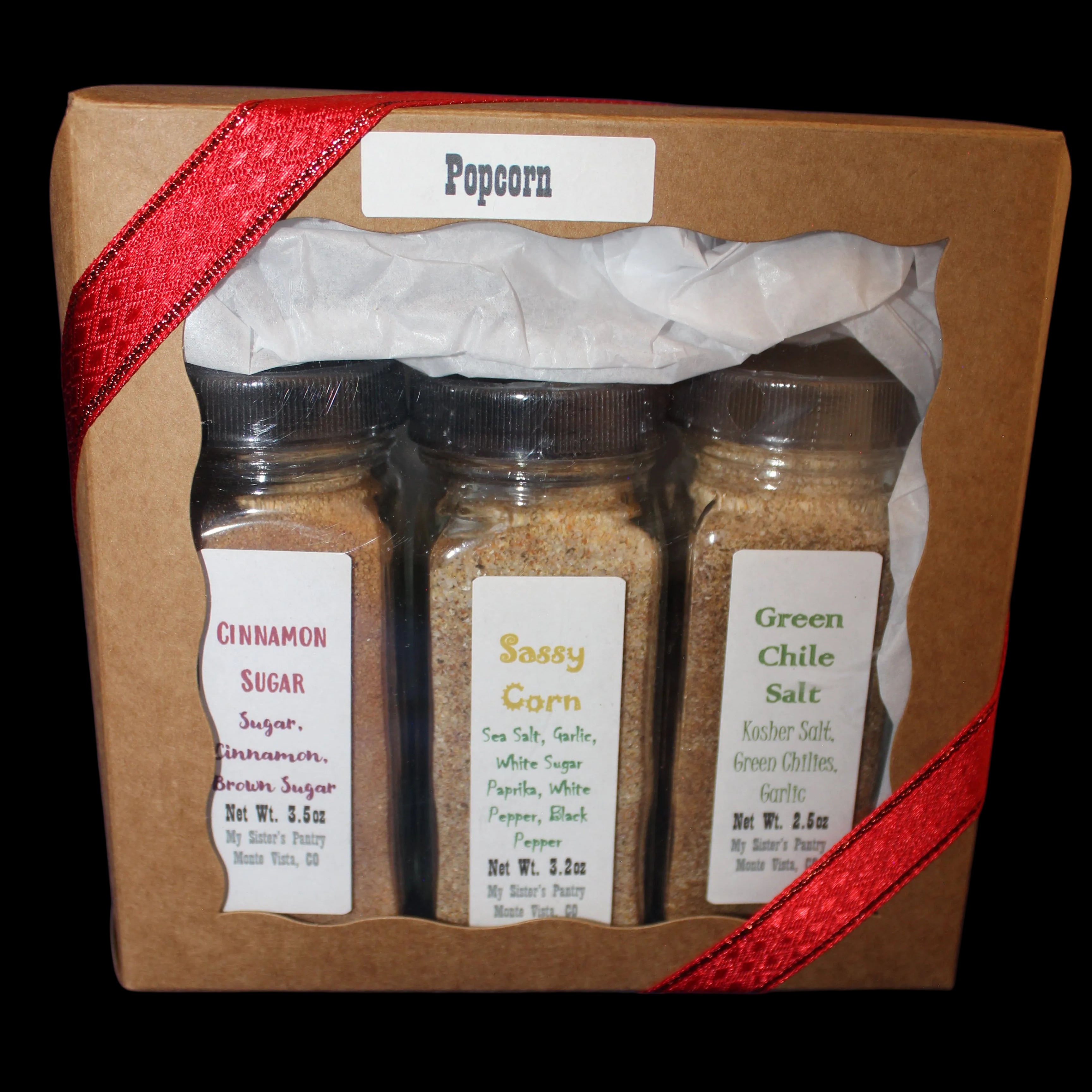 Three spice jars in a cardboard box with a red ribbon on a dark background