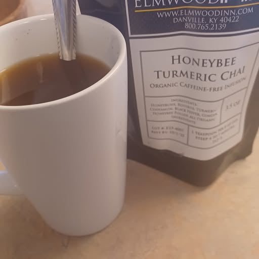 White mug with honeybee turmeric chai and a package of the product on a wooden surface