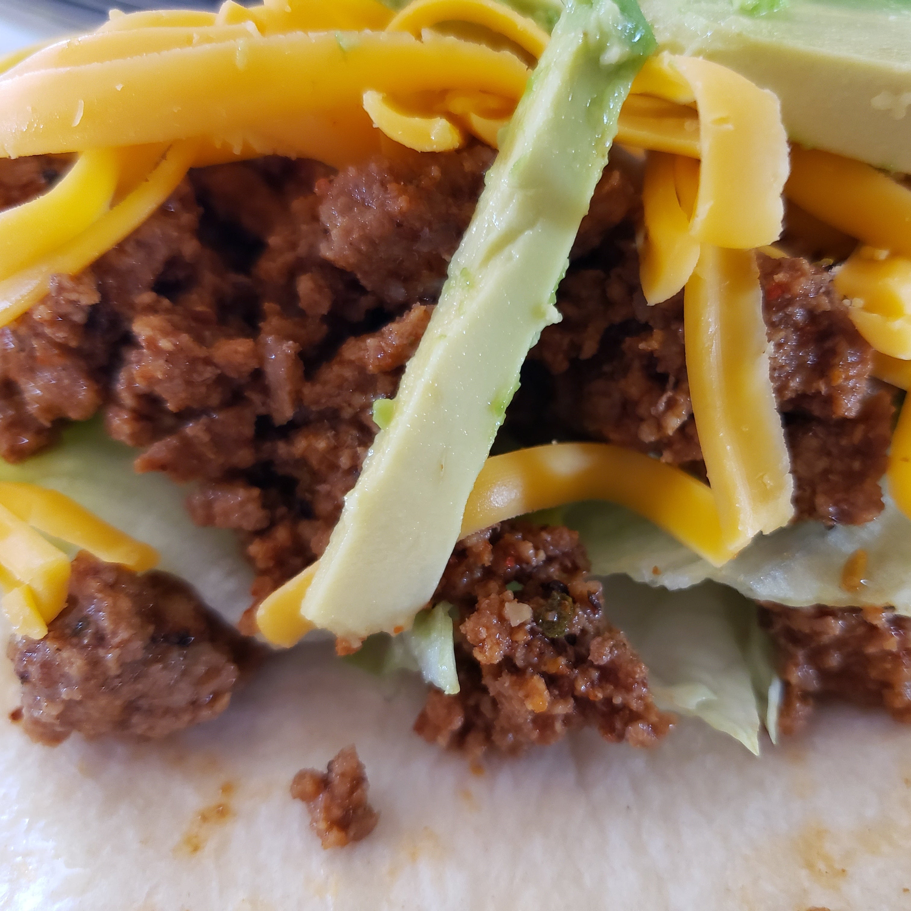 Close-up of a taco with ground beef, cheese, and avocado on a tortilla.
